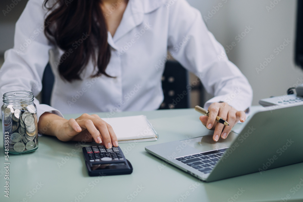 Fototapeta premium Young business woman sitting in office at table and using smartphone. On desk is laptop and tablet computer, on screen charts and graphs. Woman analyzing data. Student learning online.