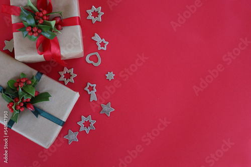 Two Christmas gifts with Holly branch with red berries and silver decorations on a red background with copy space