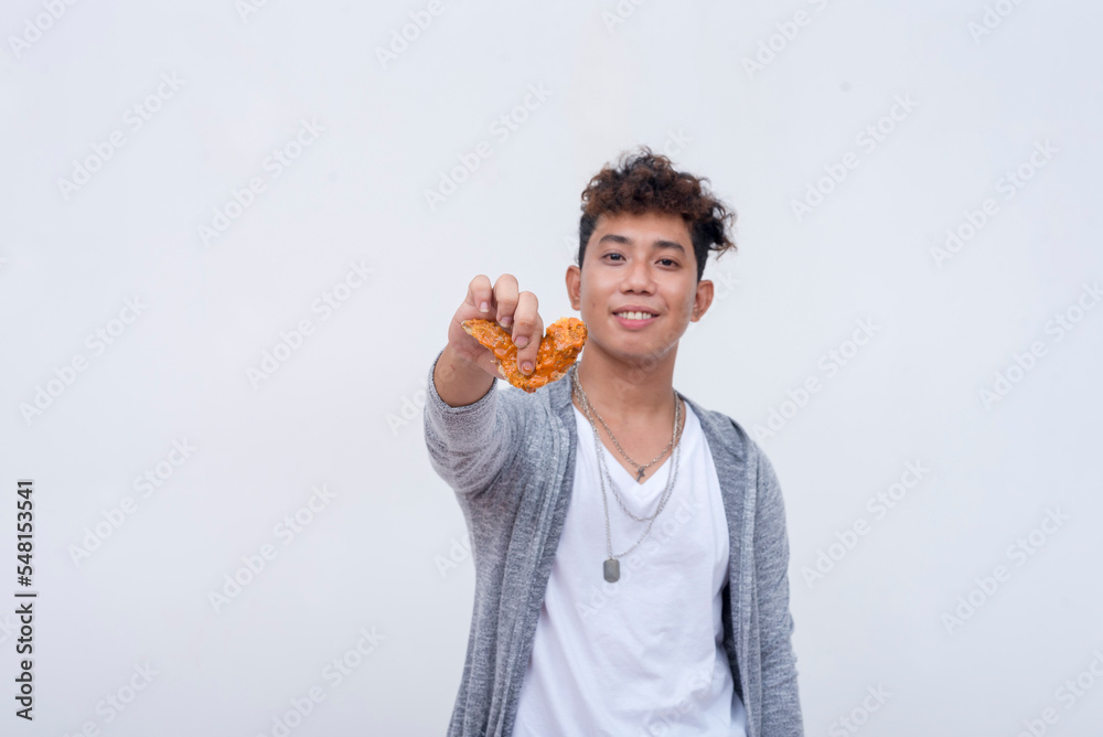 A young asian man offers a tasty chicken wing. Isolated on a light background. A young asian man offers a tasty chicken wing. Isolated on a light background.