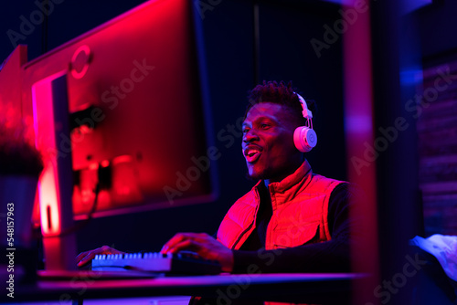 Young African man playing video game on the computer. Streamer guy sitting at home and playing another match. © JustLife