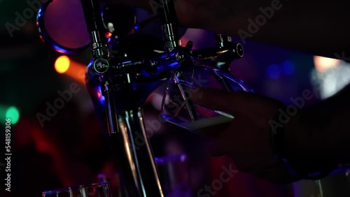 Alcoholic beverages, bartender pours beer into a glass, night club party, multicolored light. photo