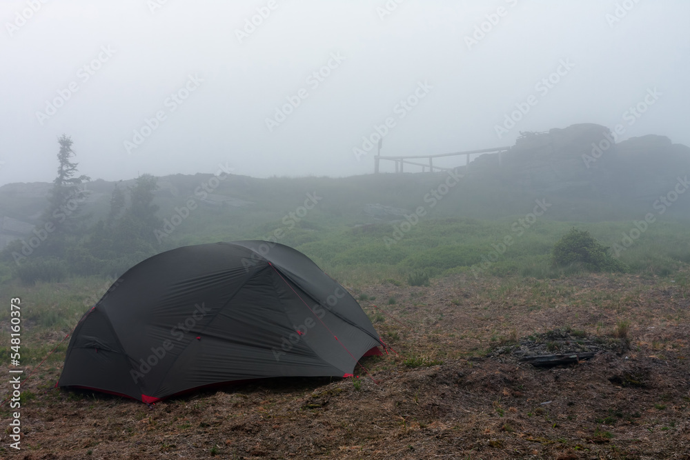 Green lightweight freestanding three-season 2-person tent on  hill in grass in the evening after rainstorm.  Jesenik mountains, Czech Republic