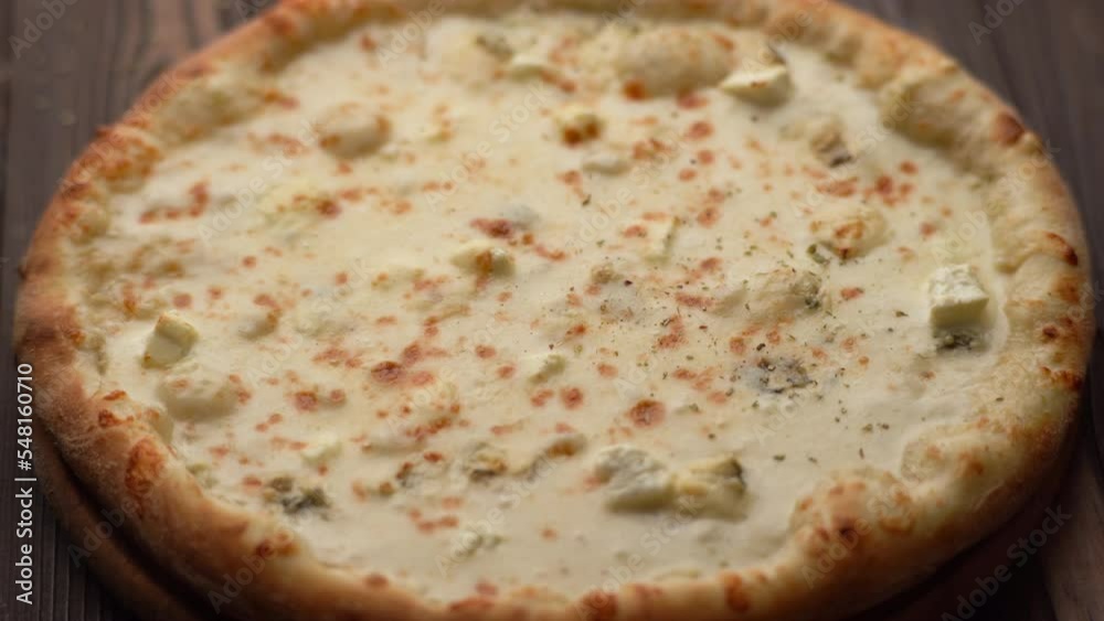 Four cheese pizza quattro formaggi with pouring herbs on a rustic wooden board background