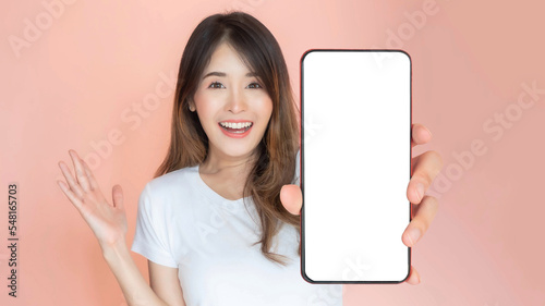 beautiful Asian young woman showing big smart phone with blank screen , white screen empty copy space for advertising banner isolated on pink background , Mock Up Image
