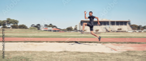 Long jump, athletics and fitness with a sports man jumping into a sand pit during a competition event. Health, exercise and training with a male athlete training for competitive track and field photo