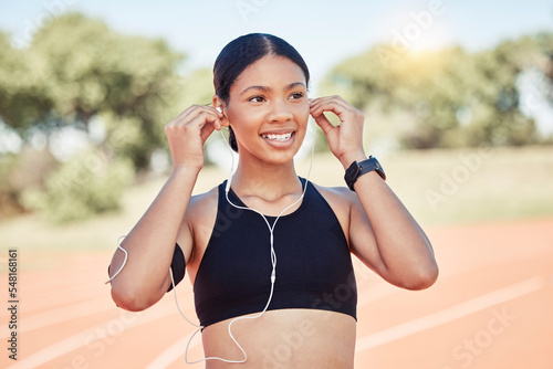 Fitness, exercise and black woman listening to music with earphones for running motivation while outdoor at stadium for marathon or race training. Smile of athlete happy before exercise or run