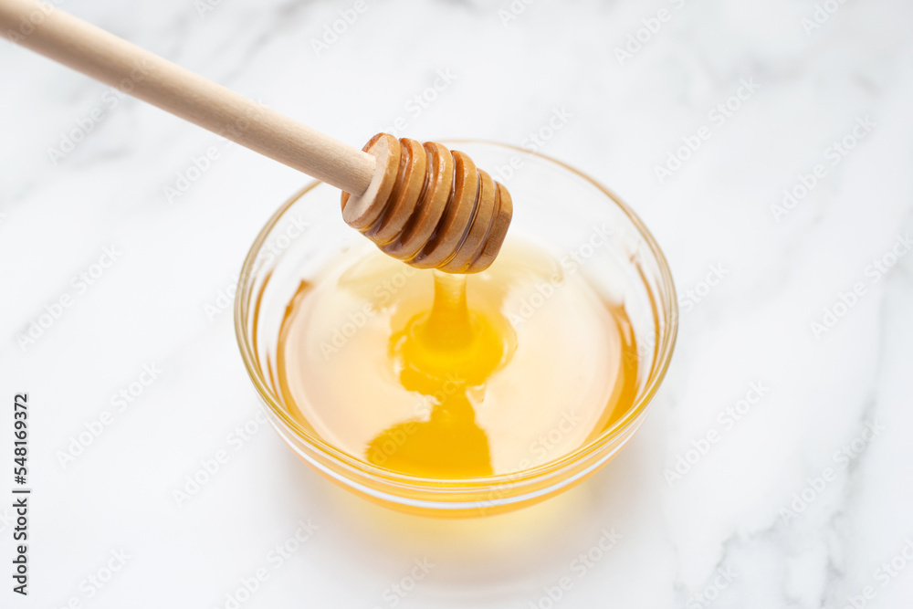 Honey flows from a wooden spoon into a glass bowl. Marble background. Honey flows from a wooden spoon into a glass bowl. Marble background.