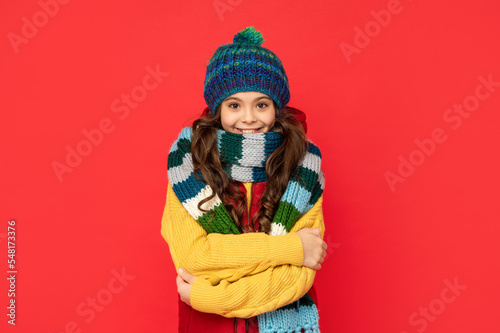 teen girl in knitted winter hat and scarf feel cold on red background, seasonal clothes