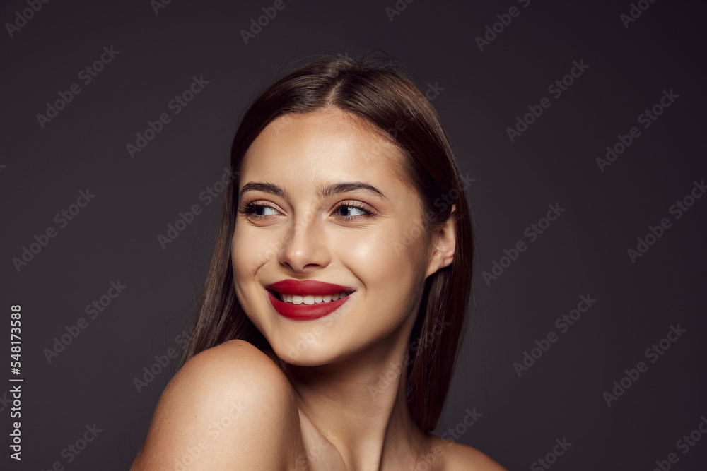 Portrait of young beautiful girl with red lips smiling, posing isolated over dark grey background. Concept of beauty, fashion and cosmetology