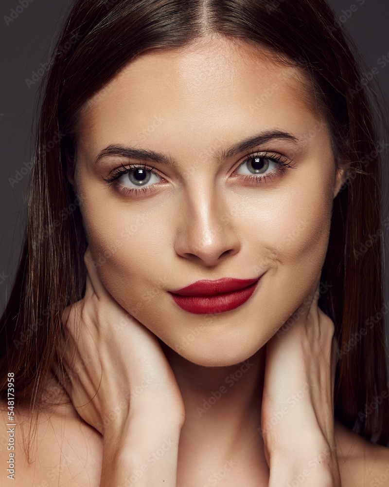Portrait of young beautiful girl posing isolated over dark grey background. Nude makeup with bright red lips. Concept of beauty, fashion and cosmetology Portrait of young beautiful girl posing isolated over dark grey background. Nude makeup with bright red lips. Concept of beauty, fashion and cosmetology