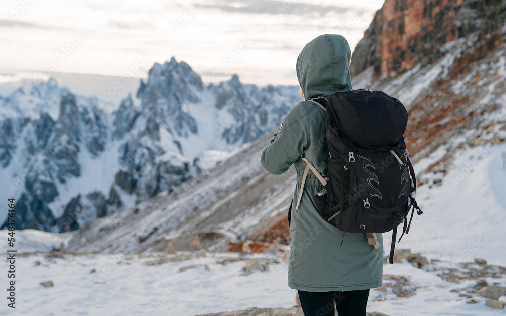 Woman hiker with knapsack look on panorama view of Dolomites mountain in Italy at sunset. Tre Cime di Lavaredo mountain.