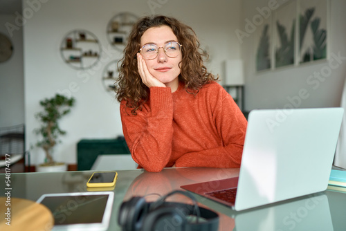Young pretty thoughtful woman student looking away thinking while working learning online on laptop computer at home taking break feeling bored, dreaming or contemplating, reflecting sitting at table.