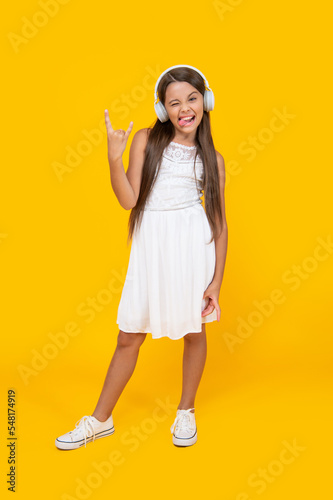 cool teen girl listen music in headphones on yellow background