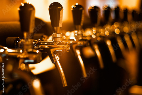 Creatively blurred image of faucets in beer pub with defocused bokeh and artistic digital noise. Golden row of taps in tap room. Bar background image