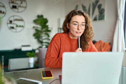 Young girl female student using laptop elearning or remote working at home office looking at computer watching webinar, learning training, studying online seminar or video calling for work meeting.