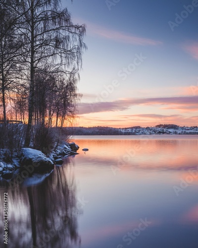 Winter lake reflecting the colors of the magical sunset surrounded by rocks and trees