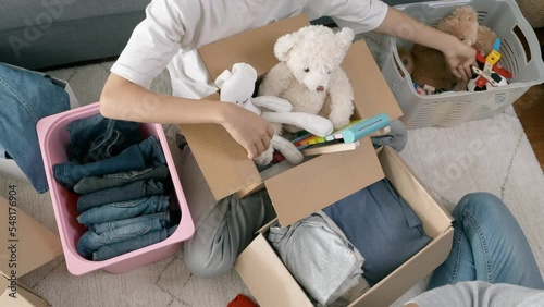 Woman and child sorting old clothes, toys and packing into cardboard boxes. Donations for charity, help low income families, declutter home, moving moving into new home, recycling, sustainable living photo