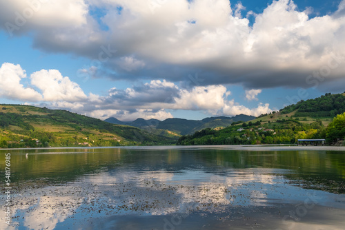 View of blue cloudy sky and wooded mountains reflected in water on a summer sunny day