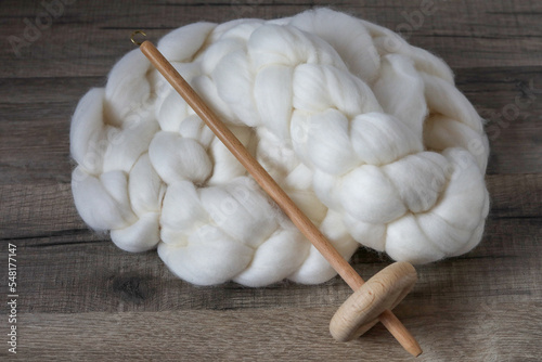 Fényképezés Wooden handspindle for spinning wool is laying on a skein of carded sheep wool on a woodden table, showcasing this traditional hobby of spinning