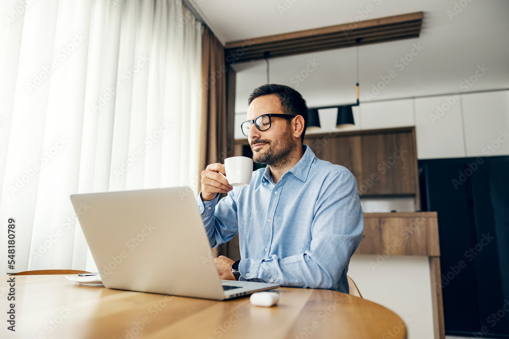 A businessman enjoying coffee at home while working on a laptop.