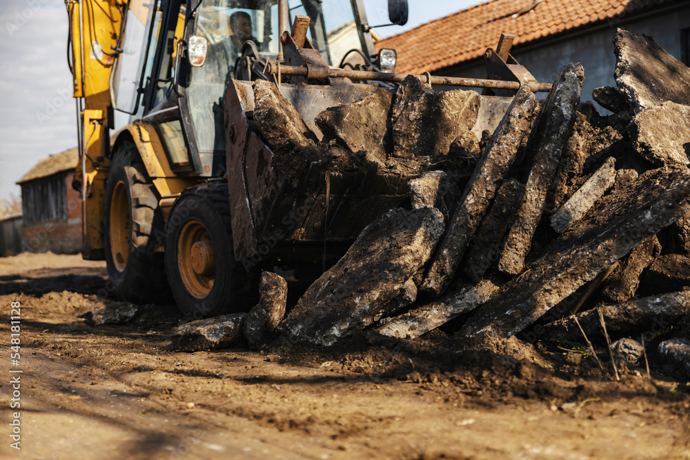 Fototapeta premium Selective focus on excavator collecting piles of asphalt on construction site.