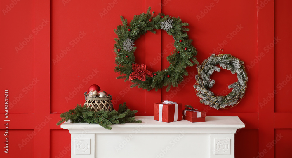 Beautiful Christmas wreaths hanging on red wall near fireplace in room Beautiful Christmas wreaths hanging on red wall near fireplace in room
