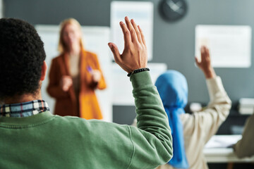 Part of back of young male student in green pullover raising hand at lesson to ask question to teacher or give his answer