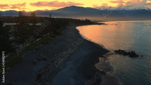 Drone shot of sea at dusk with snow capped mountain background and orange sky photo