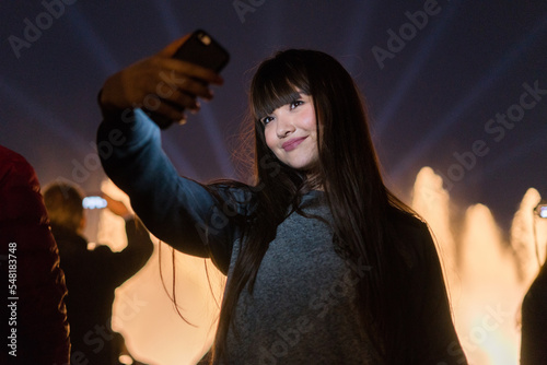 Pretty asian european girl having fun in Barcelona, in the party of the Monjuic font lights. She wears modern clothes and her hair is brunette with a fringe haircut