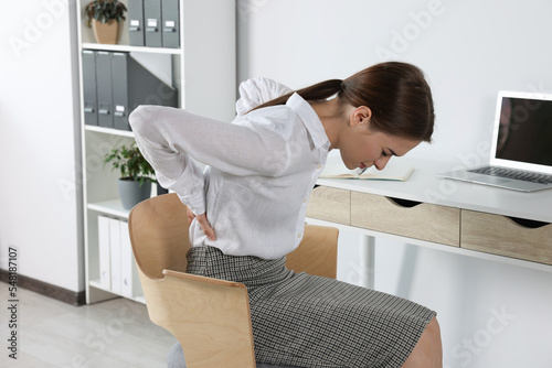 Woman suffering from back pain while sitting in office. Symptom of scoliosis photo