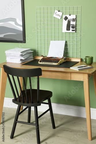 Typewriter, stack of papers and mood board on wooden table near pale green wall. Writer's workplace