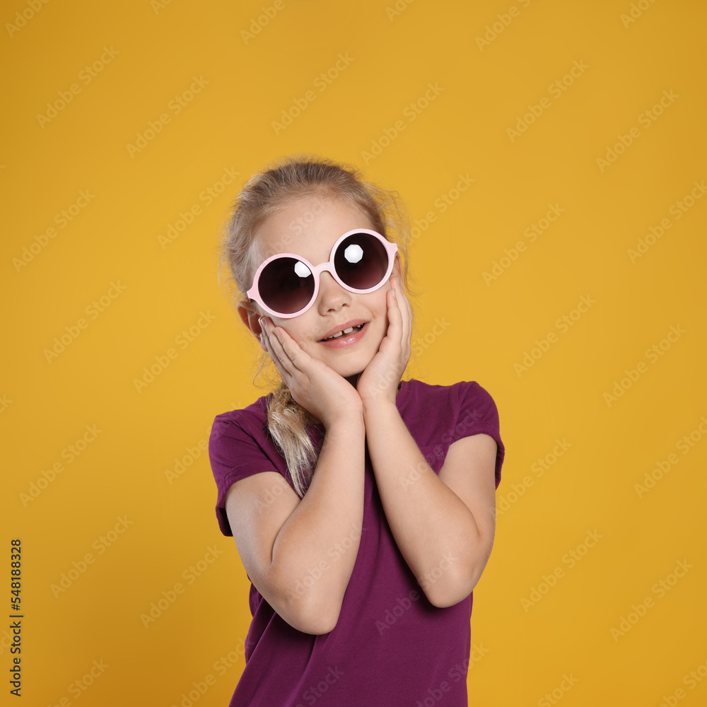 Smiling girl in stylish sunglasses on orange background