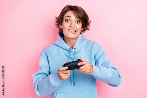 Photo of young adorable cute nice gorgeous woman wear stylish blue hoodie bite lips nervous professional gamer hold joystick isolated on pink color background