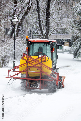 Tractor cleaning urban park paths on a cold snowy day.