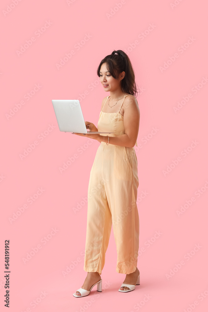 Young Asian woman using laptop on pink background - obrazy, fototapety, plakaty 