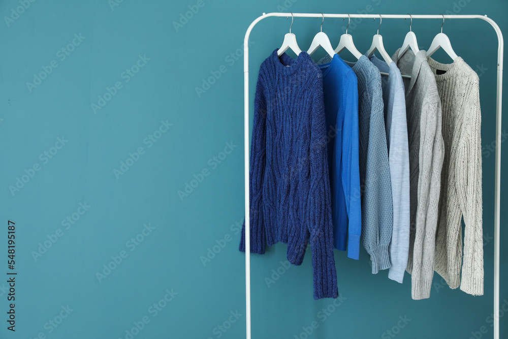 Rack with knitted sweaters near blue wall