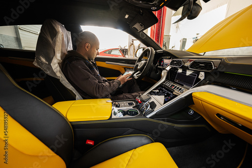 Mechanic using digital tablet, while sitting in yellow sport car suv.