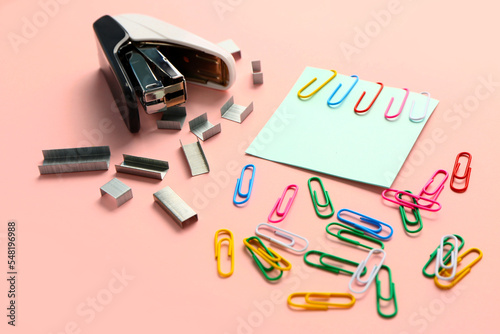 Stapler, staples and paper clips on pink background