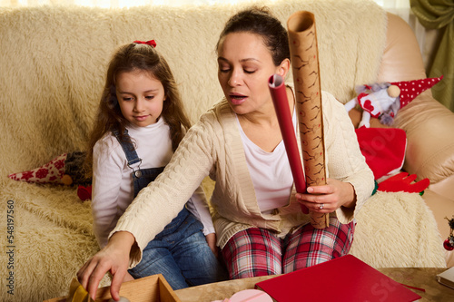 Loving mom and daughter enjoy the upcoming winter holidays, packing unwrapping Christmas New Year presents gift boxes at home together. Merry Christmas and Happy New Year! Holiday and family event photo