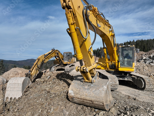 Industrial mine excavators are digging the soil in the construction site and loading trucks. Aerial drone top view. 