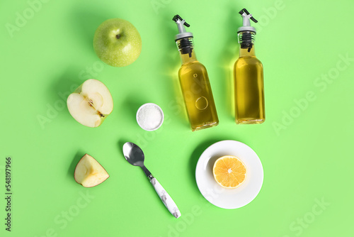 Composition with bottles of apple cider vinegar, fruits and salt on green background