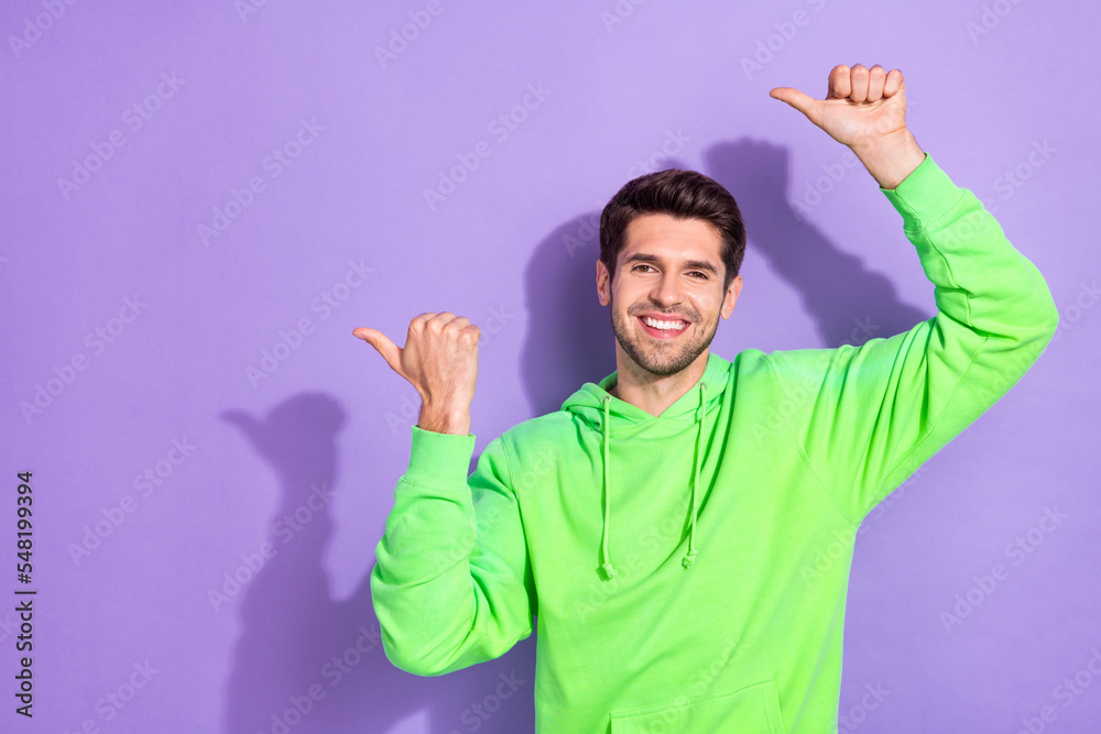 Portrait of good mood funny handsome guy with brunet hairdo wear green hoodie directing empty space isolated on violet color background Portrait of good mood funny handsome guy with brunet hairdo wear green hoodie directing empty space isolated on violet color background