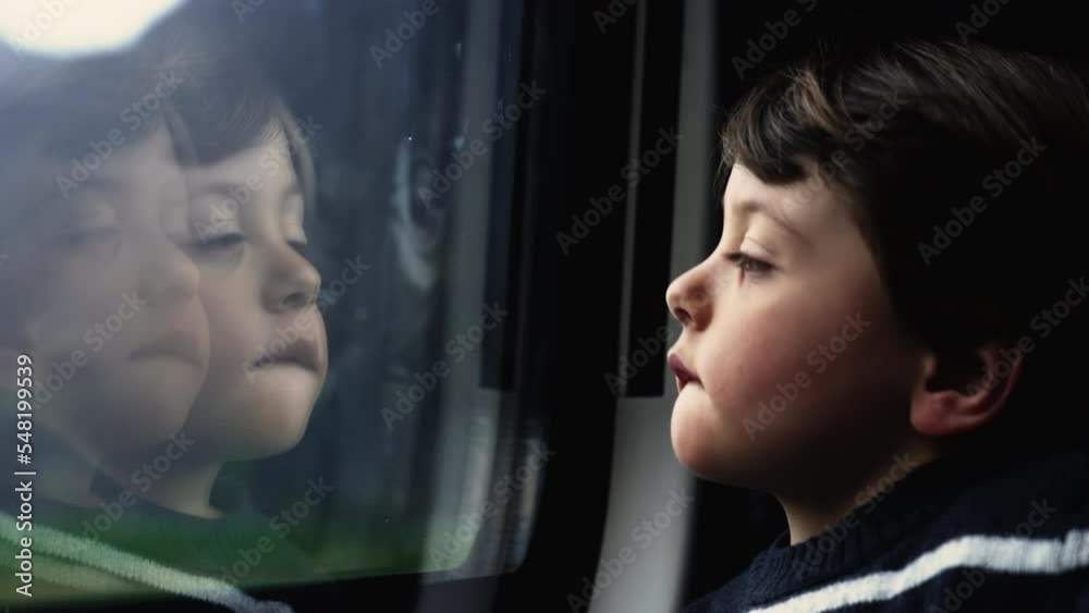 Passenger child by train window reflection. One little boy traveling looking at landscape passing by. Pensive kid