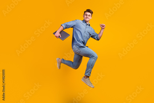 Photo of cheerful caucasian smart young man holding laptop smiling jumping high running isolated shine background