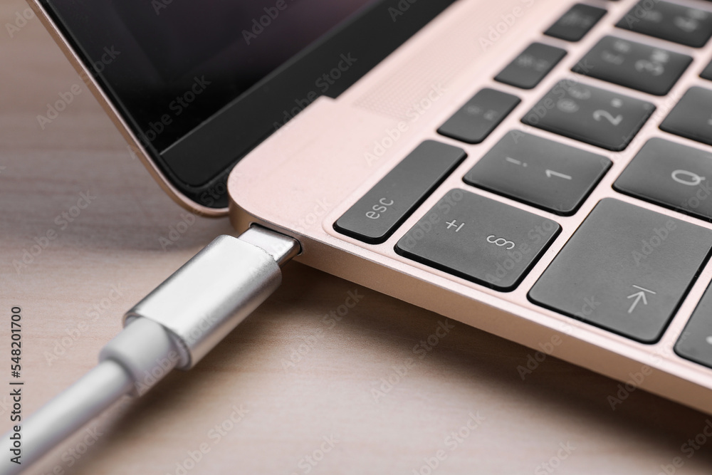USB cable plugged into laptop port on light wooden table, closeup USB cable plugged into laptop port on light wooden table, closeup
