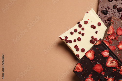 Different chocolate bars with freeze dried fruits on beige background, flat lay. Space for text