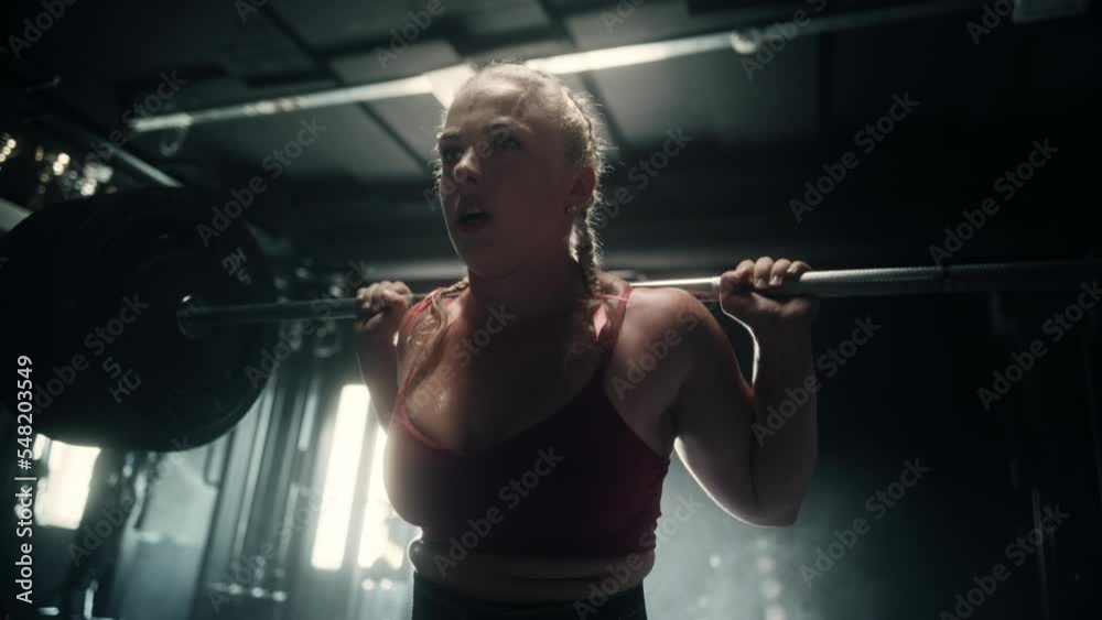 A Focused Female Bodybuilder Lifting Heavy Barbell, Exercising her Back While Doing Squats in a Hardcore Gym. A Strong Woman Training, Powerlifting and Working on Her Endurance for Championship A Focused Female Bodybuilder Lifting Heavy Barbell, Exercising her Back While Doing Squats in a Hardcore Gym. A Strong Woman Training, Powerlifting and Working on Her Endurance for Championship