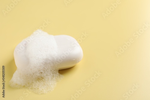 Soap with fluffy foam on yellow background, space for text