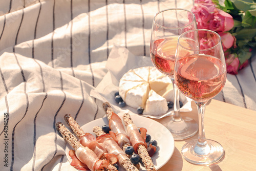 Fototapeta Naklejka Na Ścianę i Meble -  Glasses of delicious rose wine, flowers and food on picnic blanket outdoors