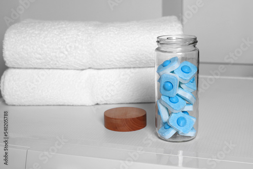 Glass jar with water softener tablets on washing machine in bathroom, space for text photo